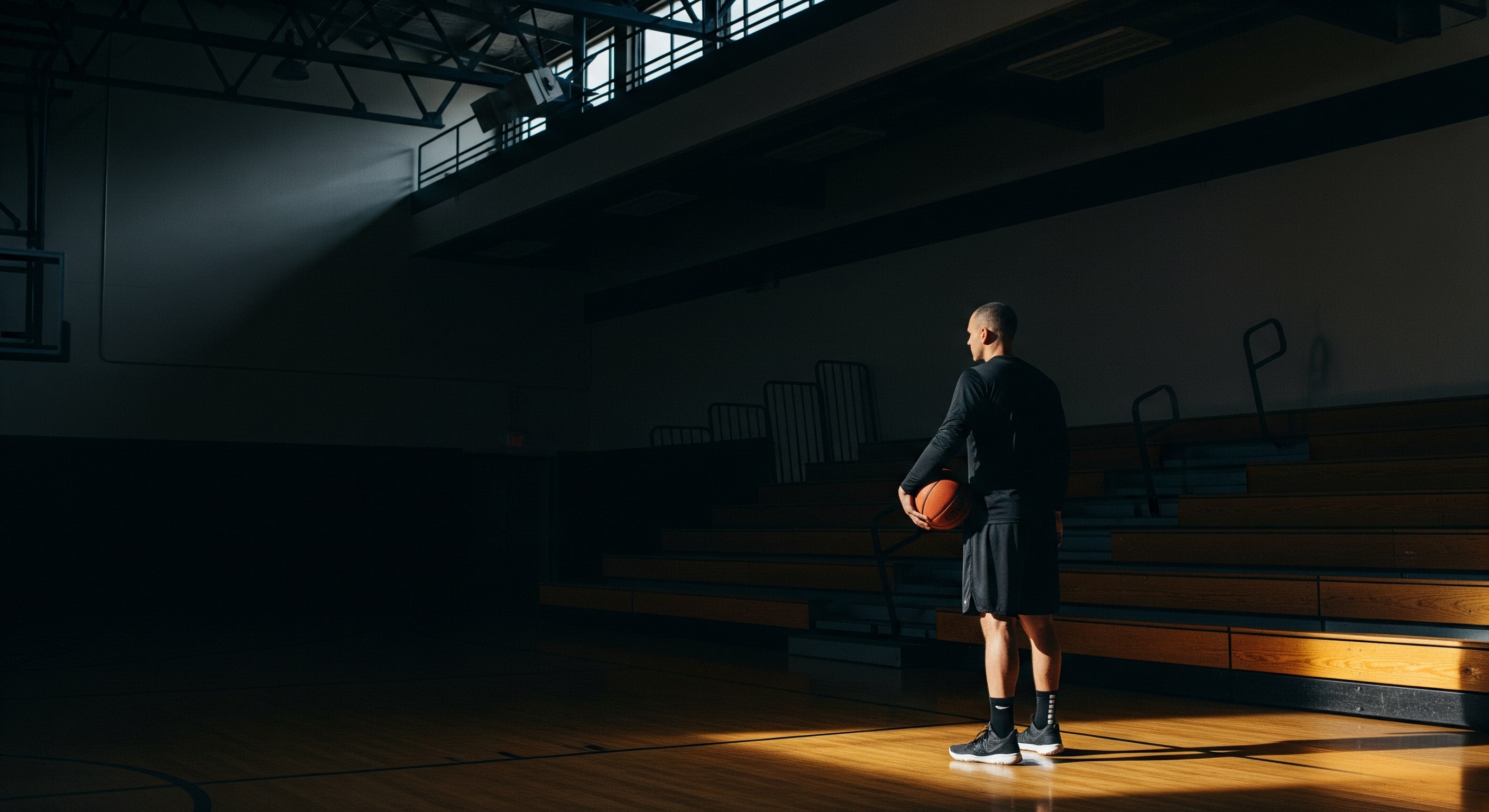 Adult athlete in a dark gym holding a basketball